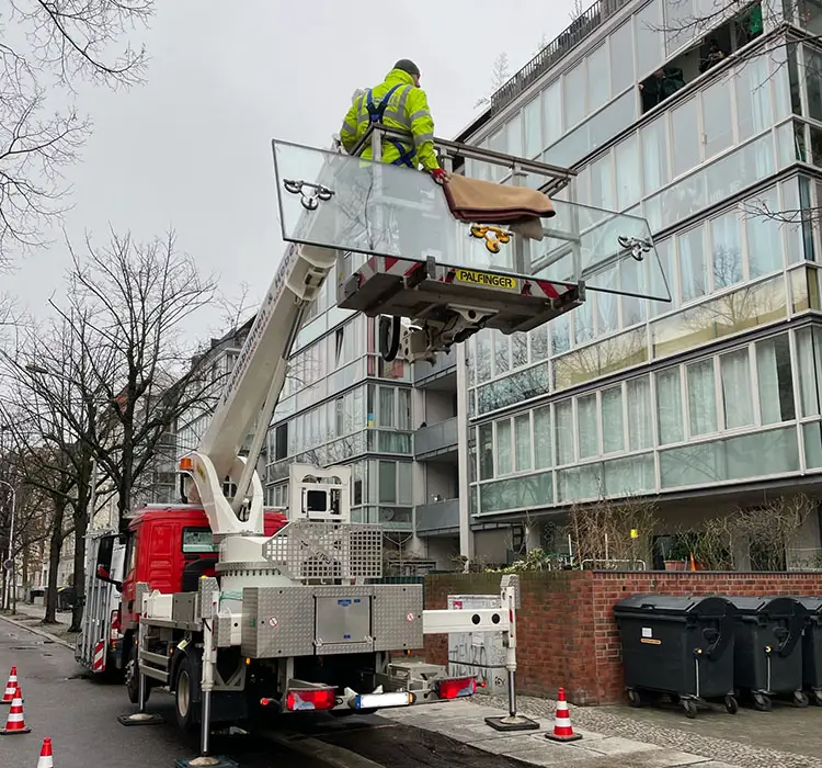 Monteur auf einer Hebebühne transportiert eine große Glasscheibe an der Fassade eines Mehrfamilienhauses